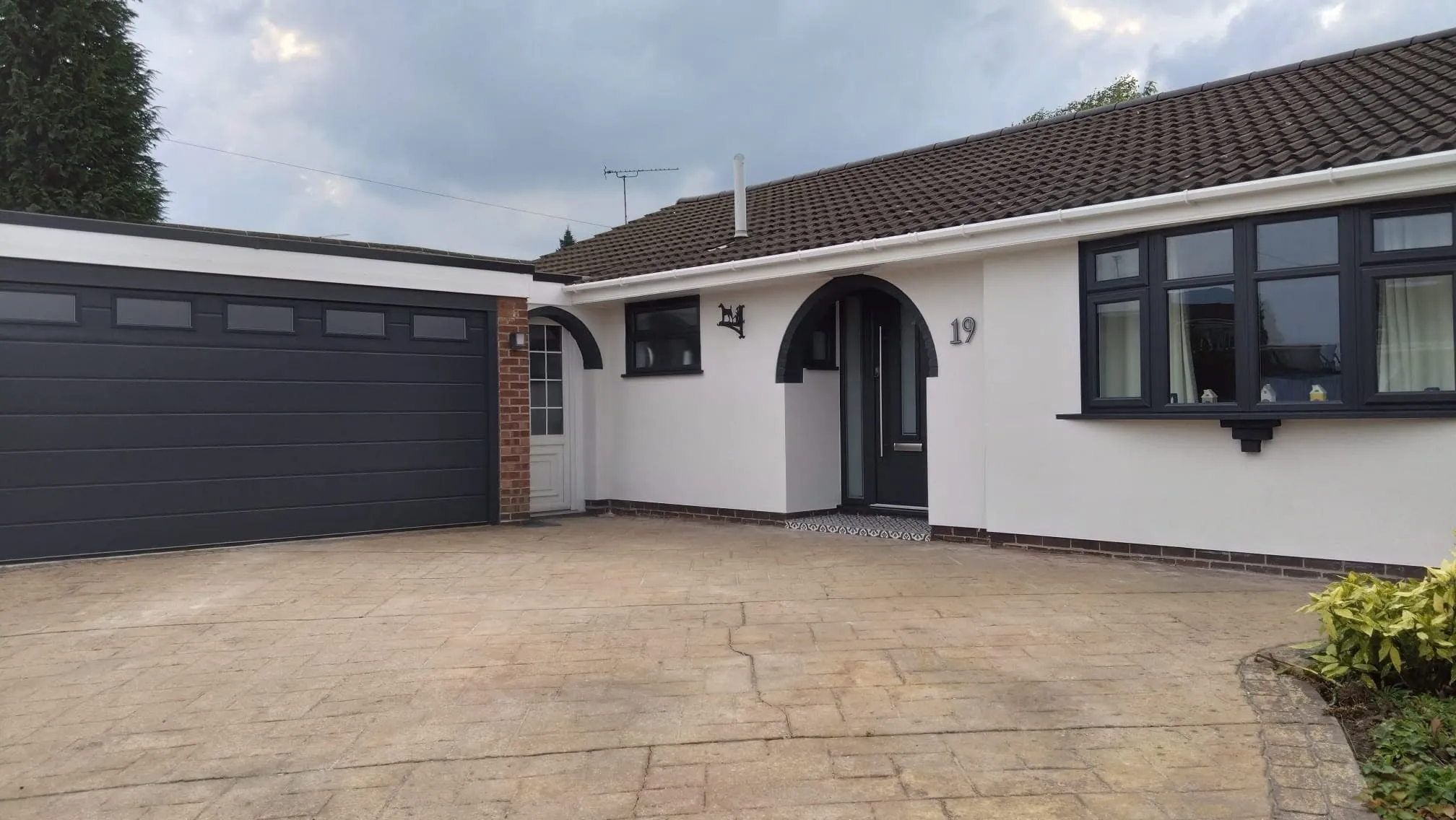 The same bungalow after rendering: a clean, uniform white finish with dark grey windows, garage door and arched porch.