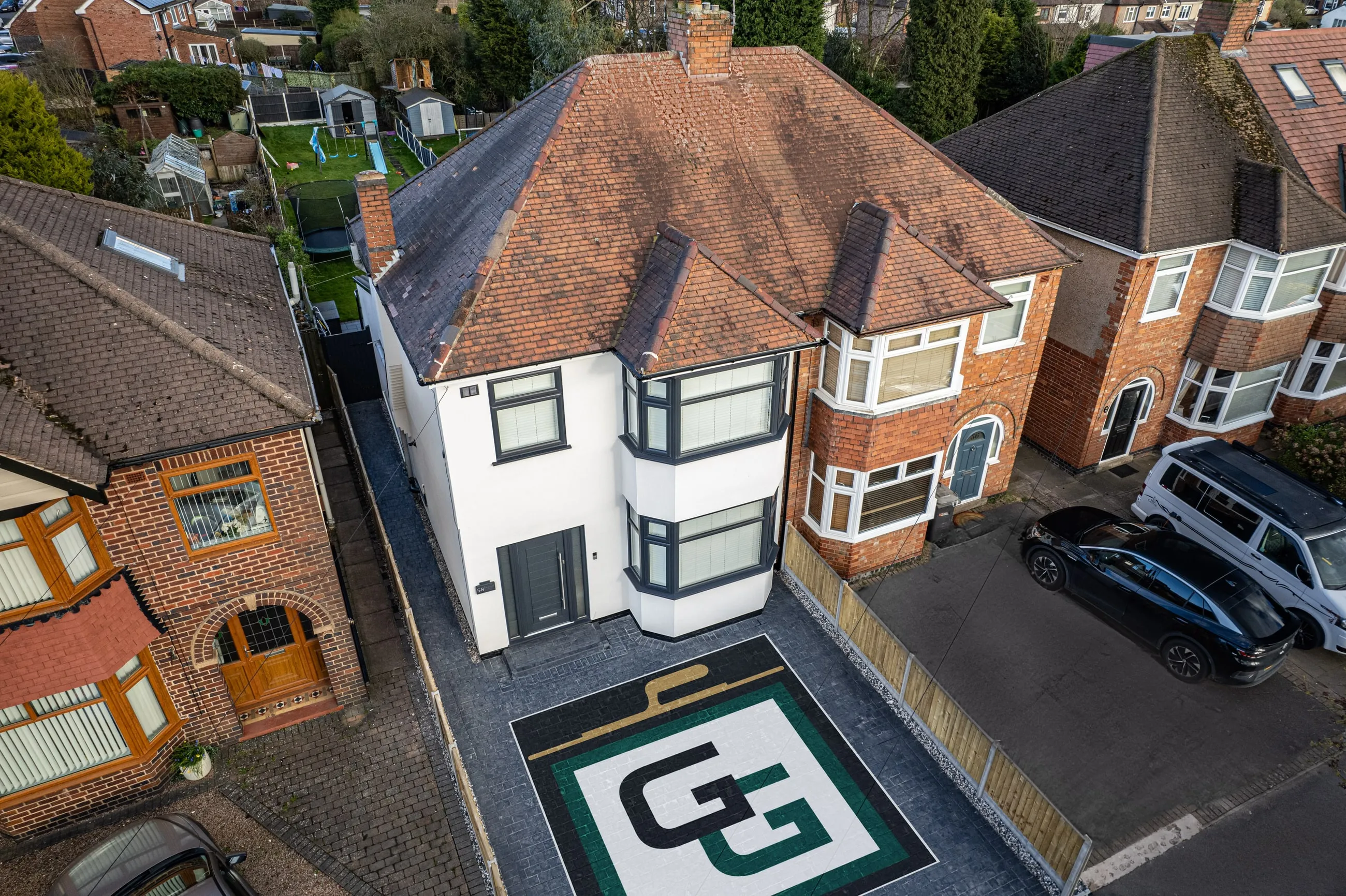 An aerial view of a house on Newdigate Road finished in white monocouche render, with the G Green GG monogram laid into the driveway below it.
