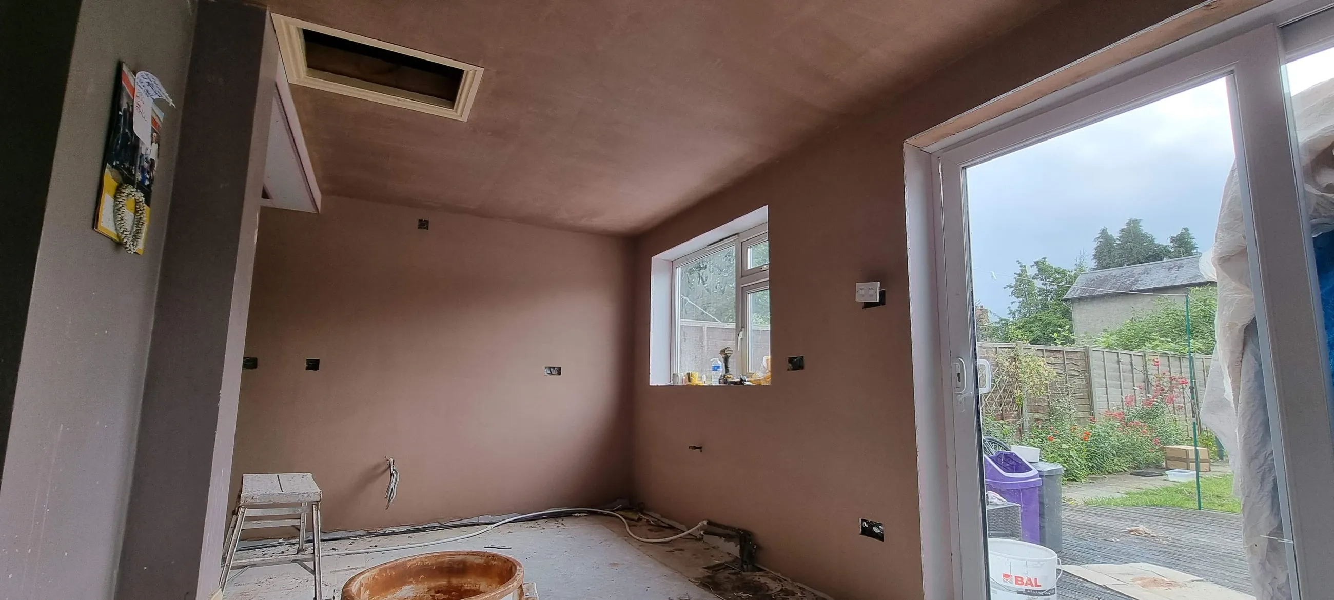A newly plastered room with a wide opening to the garden, walls and ceiling finished flat and ready to decorate.