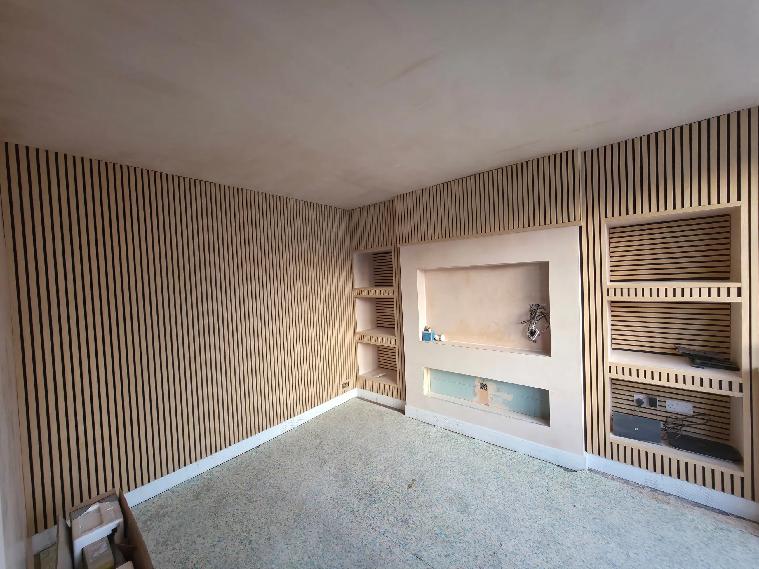 A finished room with floor-to-ceiling slatted panelling running into the corner, beside plastered alcoves and shelving.