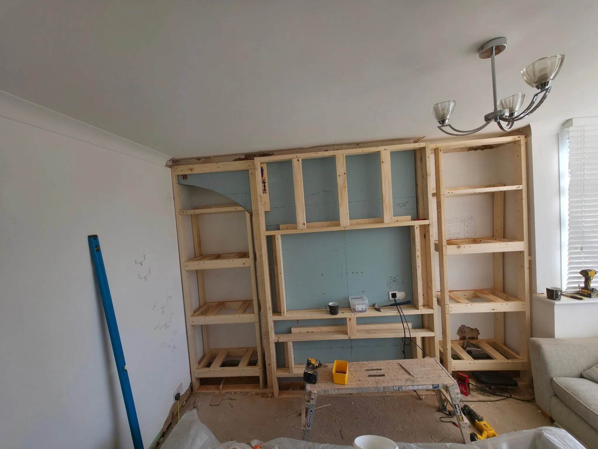 A media wall under construction: a bare timber stud frame with shelving openings, insulation board behind, and setting-out measurements pencilled on the wall alongside.