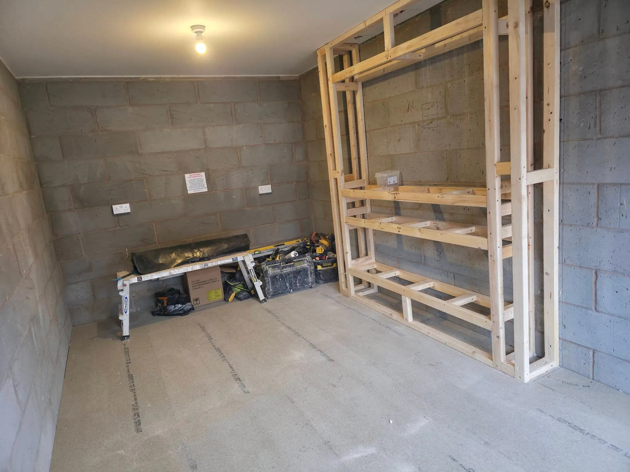 A bare blockwork garage mid-conversion, with a timber media wall frame built against the far wall.