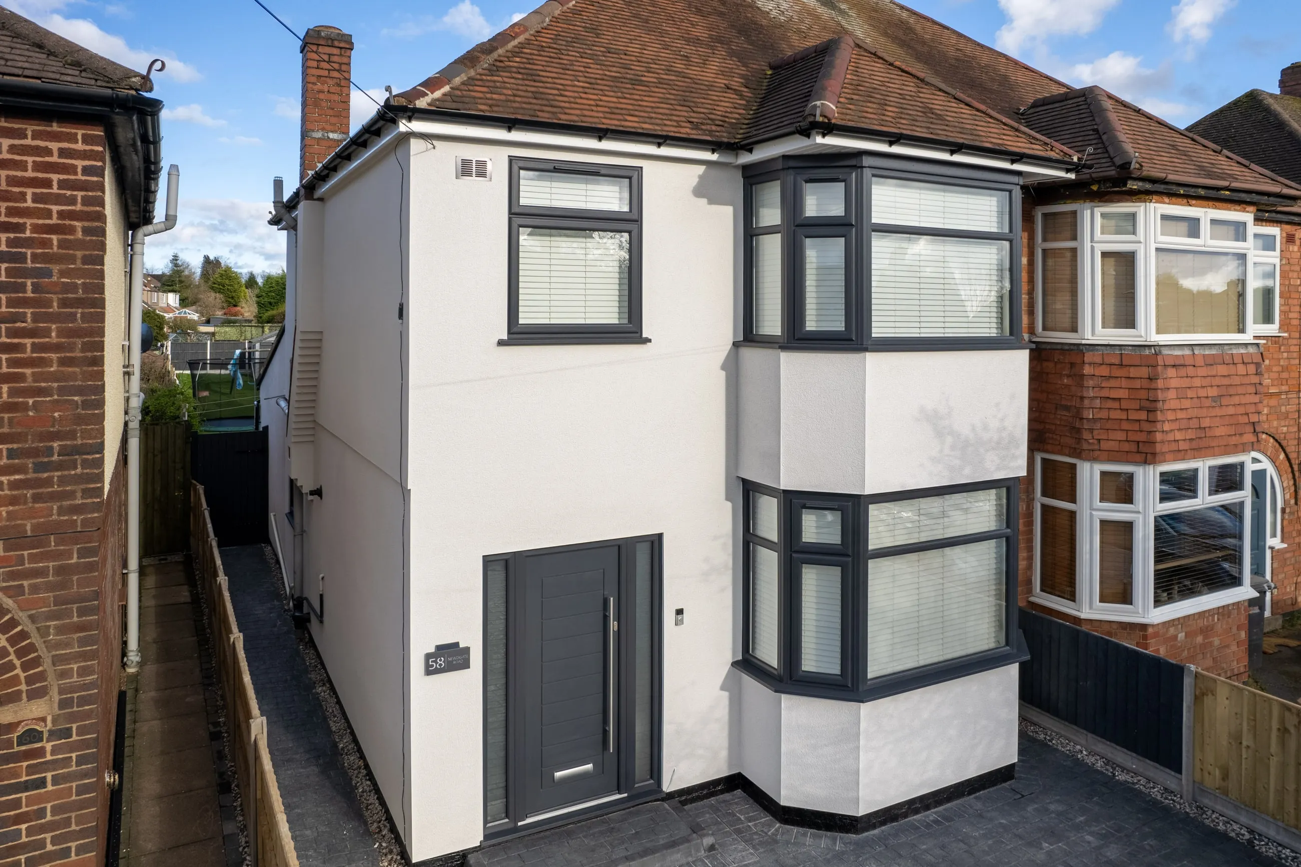 A 1930s semi-detached house finished in white monocouche render, with a two-storey bay window and dark grey window frames, against a blue sky.