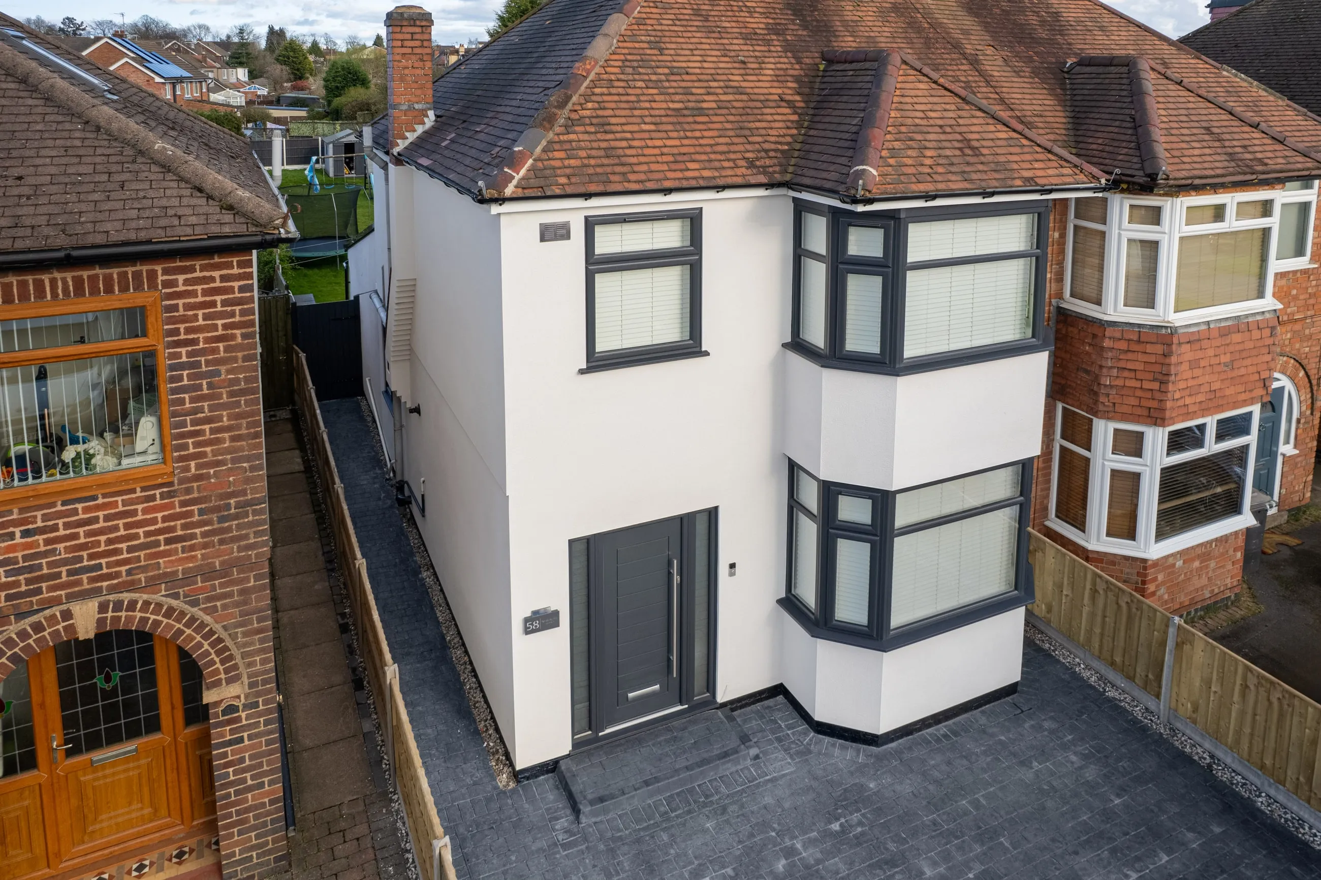 The monocouche-rendered house from the side, showing the bay and the clean junction where render meets the neighbouring brickwork.