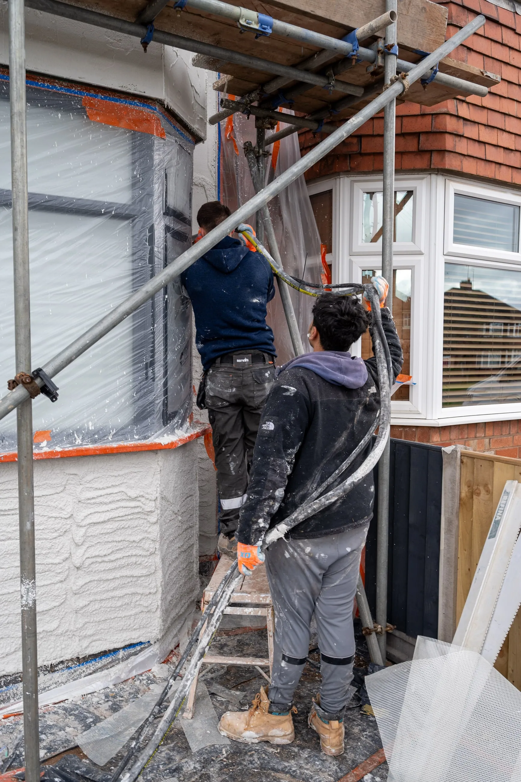 Two of the team applying render to a bay window elevation from a scaffold, the surface half finished.