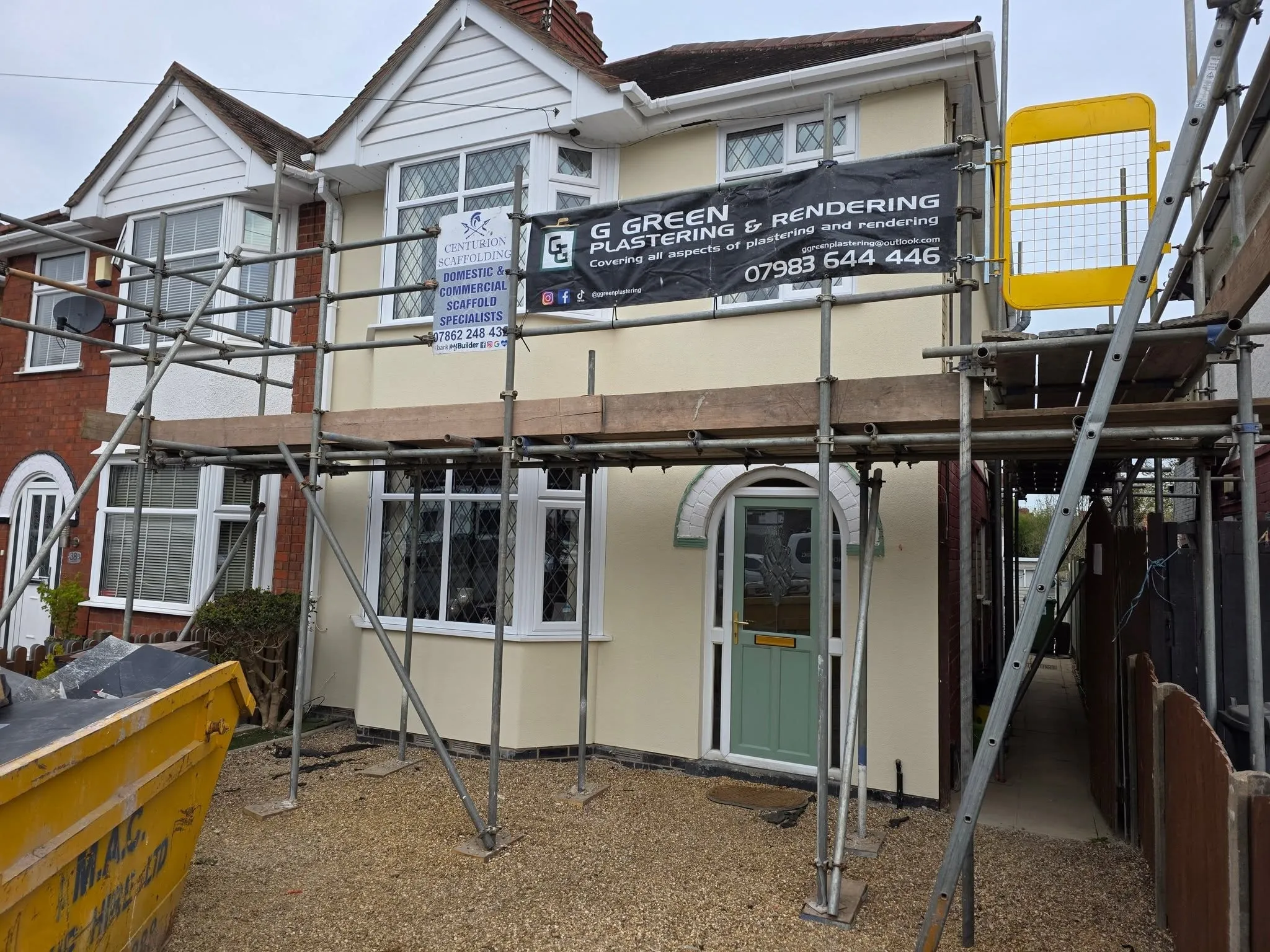 A semi-detached house rendered in cream, scaffolding still up and a G Green Plastering & Rendering banner fixed across it.