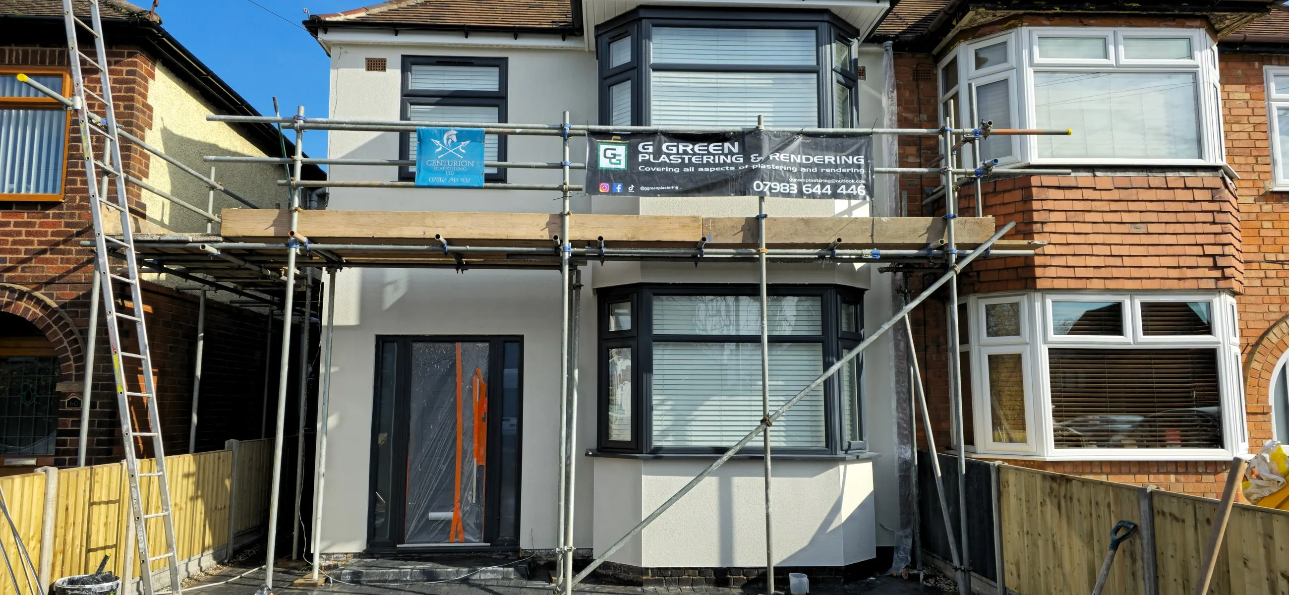 A wide panoramic view of a rendered semi-detached house with scaffolding across the full frontage.